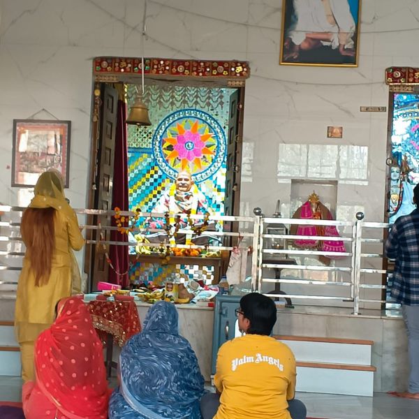 Delhi ke Neem Karoli Baba mandir me darshan aur prarthana karte hue bhakt, samne Maharaj ji ki sundar murti aur rangeen sajawat.
