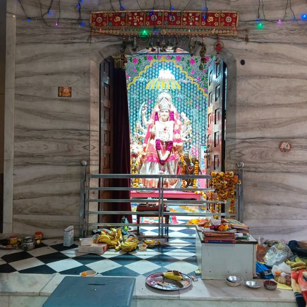 Neem Karoli Baba mandir Delhi me Mata Rani ki bhagya murti aur sundar darbar, jahan bhakton dwara chadhaaye gaye phool aur prasad rakhe hain.