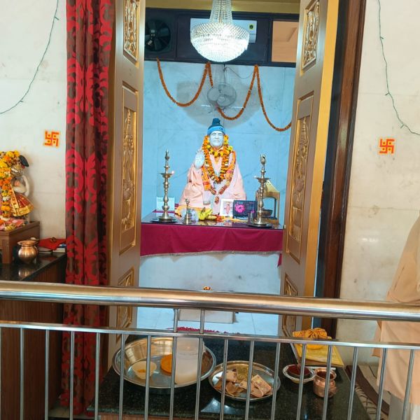 Delhi ashram me Neem Karoli Baba ki safed sangmarmar ki murti, jisme unhone apna chola aur topi pehni hui hai aur phoolon ki mala se saje hain.